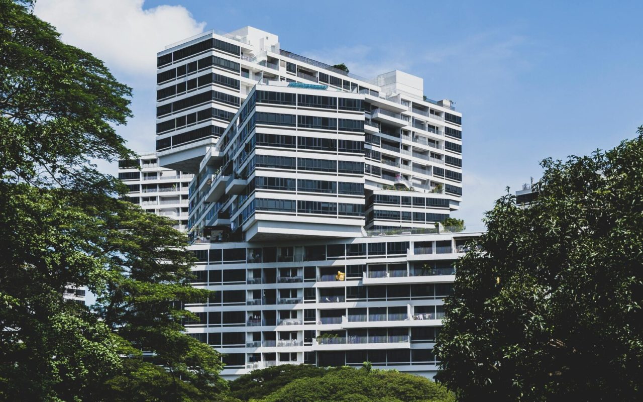 Contemporary apartment buildings in verdant Singapore landscape under a clear blue sky.