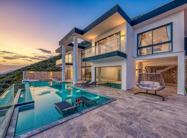 Elegant modern villa featuring an infinity pool and scenic hill views during sunset.