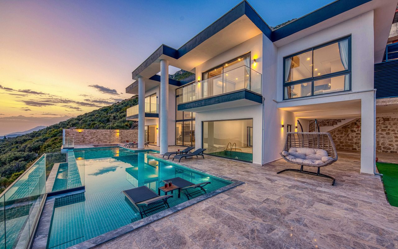Elegant modern villa featuring an infinity pool and scenic hill views during sunset.