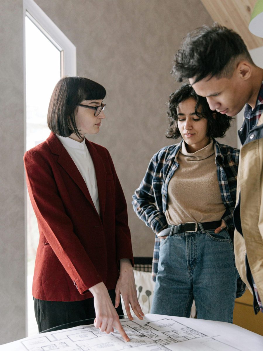 A real estate agent discusses home plans with a couple in a modern office setting.